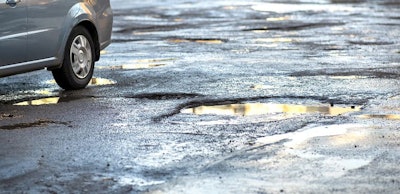 Close up of car wheel on a road in very bad condition with big potholes full of dirty rain water pools.