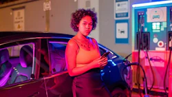 Pretty girl with smartphone standing by electric car
