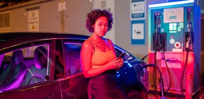 Pretty girl with smartphone standing by electric car