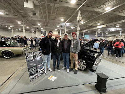 Classic Chevrolet display at automotive event with four enthusiasts beside restored black car