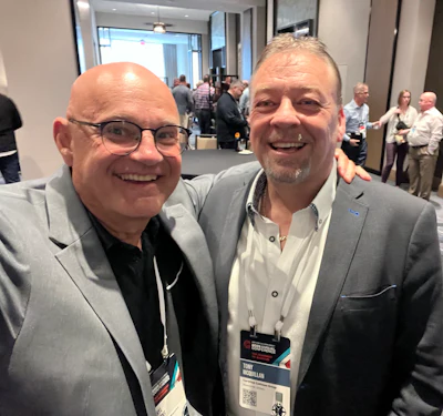 Two colleagues networking at a professional conference, wearing gray blazers and conference badges