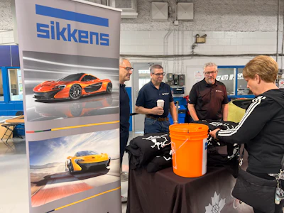 Sikkens automotive paint display with McLaren supercars and technical professionals in workshop