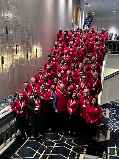 Large team in red corporate jackets posing together on a contemporary staircase