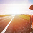 Orange sports car on highway with sunlit fields and distant towers