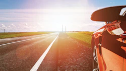 Orange sports car on highway with sunlit fields and distant towers