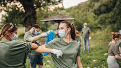 Volunteers in masks cleaning outdoor green space, wearing matching green shirts
