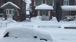 Snow-covered suburban street with buried car during intense winter storm