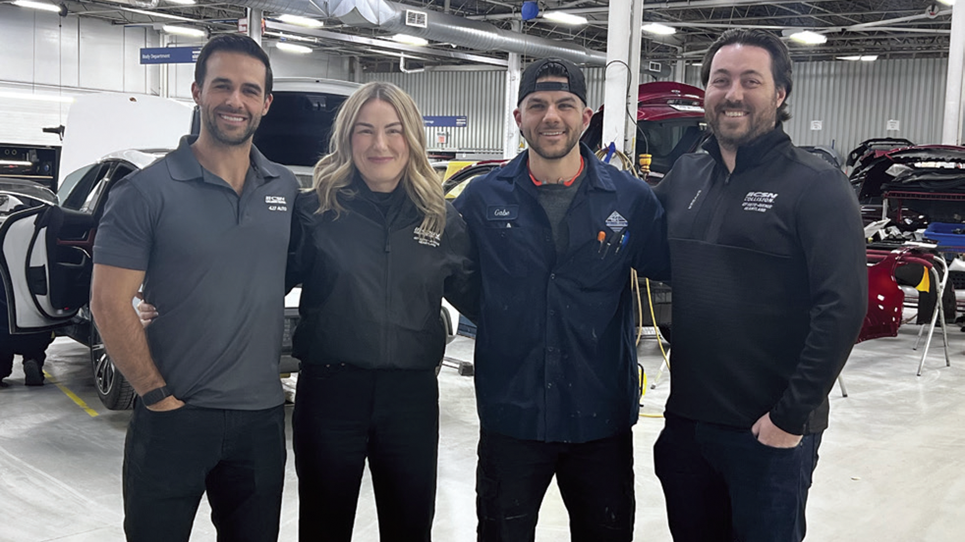 Automotive service team posing together in professional workshop with vehicles