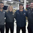 Automotive service team posing together in professional workshop with vehicles