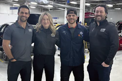 Automotive service team posing together in professional workshop with vehicles