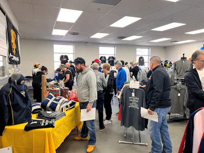 Crowded merchandise event with people browsing shirts and apparel on yellow display table