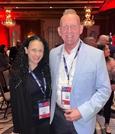 Two professionals at conference networking event, wearing event badges in elegant chandelier-lit room
