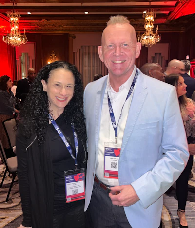 Two professionals at conference networking event, wearing event badges in elegant chandelier-lit room