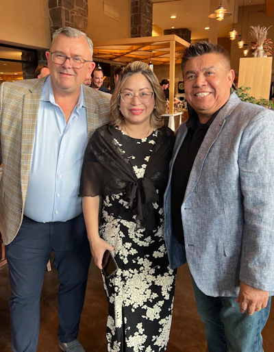 Three professionals in business attire smiling together at an elegant indoor venue