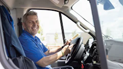Smiling delivery driver in blue shirt seated in commercial van