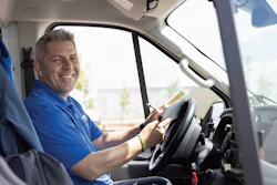 Smiling delivery driver in blue shirt seated in commercial van