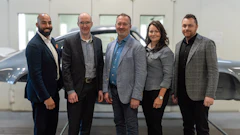 Professional automotive team in business attire posing in modern vehicle facility