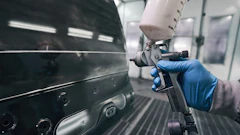 Auto body technician spraying paint on vehicle panel with professional spray gun