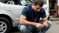 Mechanic crouching beside car, carefully examining or repairing vehicle equipment