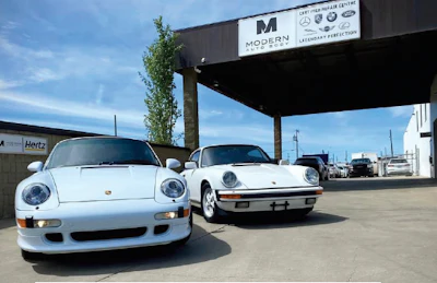 Two vintage white Porsche 911 sports cars parked at automotive service center