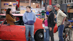 Multigenerational group standing near classic red car in automotive workshop