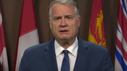 Government official speaking at press conference with Canadian provincial flags