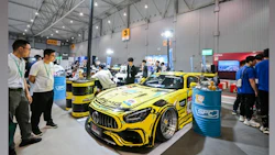 Yellow Mercedes-AMG racing car displayed at automotive trade show with industrial backdrop
