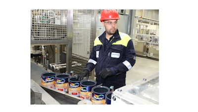 Factory worker monitoring Dulux paint can production line with safety equipment