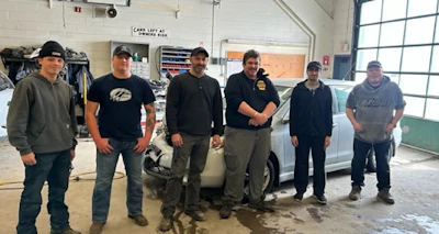 Auto repair team of six workers standing together in garage workshop beside white car