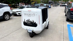 Brooklyn Pizza autonomous delivery vehicle with city skyline graphic in urban parking lot
