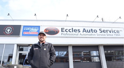 Automotive technician at Eccles Auto Service storefront, wearing dark jacket and cap