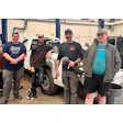 Auto repair team of four technicians standing together in service garage workspace