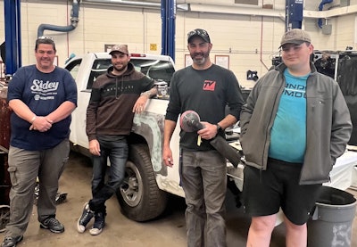 Auto repair team of four technicians standing together in service garage workspace