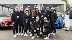 Corporate team in matching black uniforms posing with vehicles at outdoor event