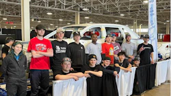 Automotive students pose with white vehicle in technical training workshop