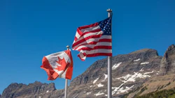 Canadian and US flags flying with rocky mountain landscape in background