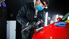 Professional auto detailer polishing a red car with orbital buffer