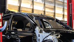 Severely damaged black vehicle in auto repair garage, exposed frame and body panels