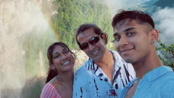 Three smiling people posing together with a misty mountain and waterfall backdrop