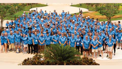 Large corporate team in blue tropical shirts posing for group photo outdoors