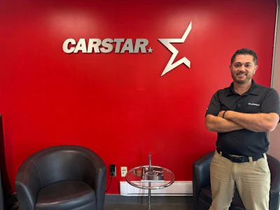 CARSTAR logo on red wall with employee standing nearby