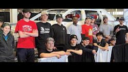 Diverse team of young technicians posing in automotive workshop with training vehicle