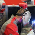 Welder in protective mask and red-gray suit performing welding with bright blue spark