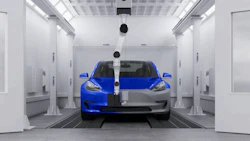 Blue Tesla electric vehicle positioned in a white paint testing chamber
