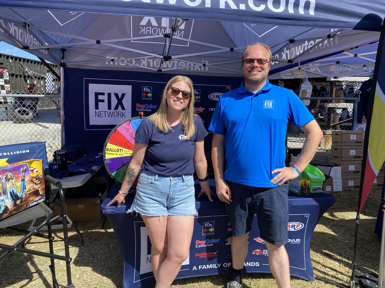 Fix Network booth with two employees at outdoor event under branded tent