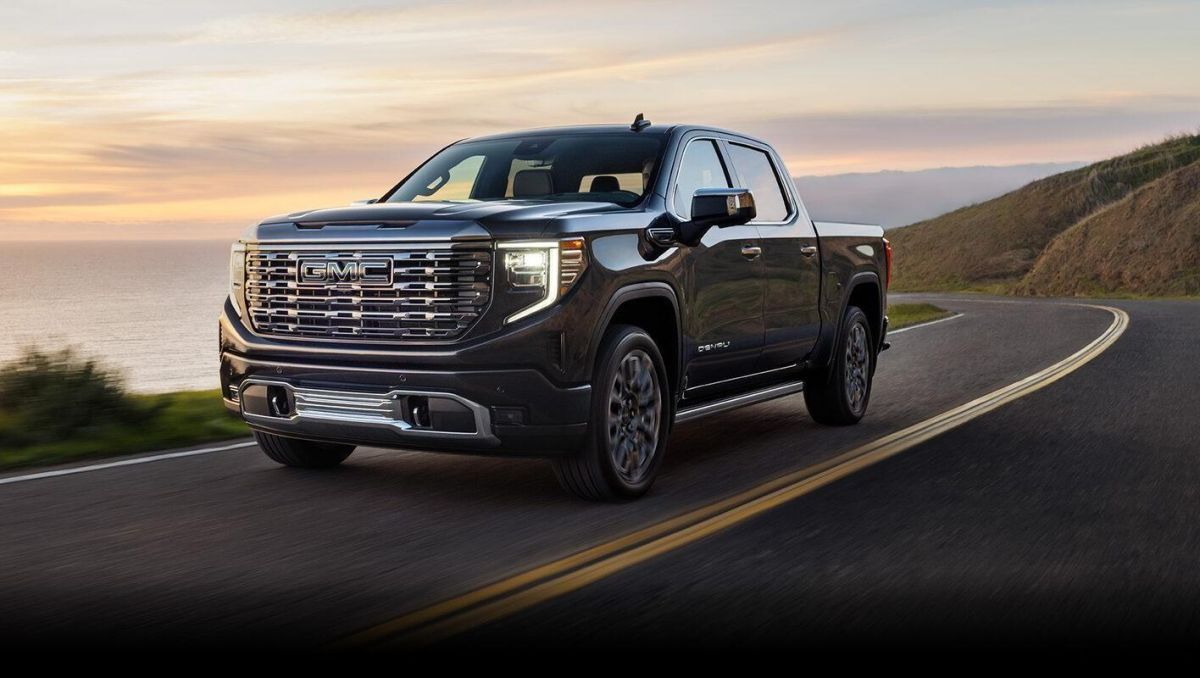Black GMC Sierra pickup truck driving on coastal highway at sunset