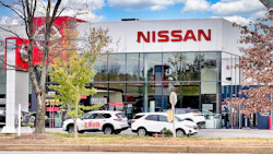 Nissan car dealership with white vehicles parked in front of modern glass showroom