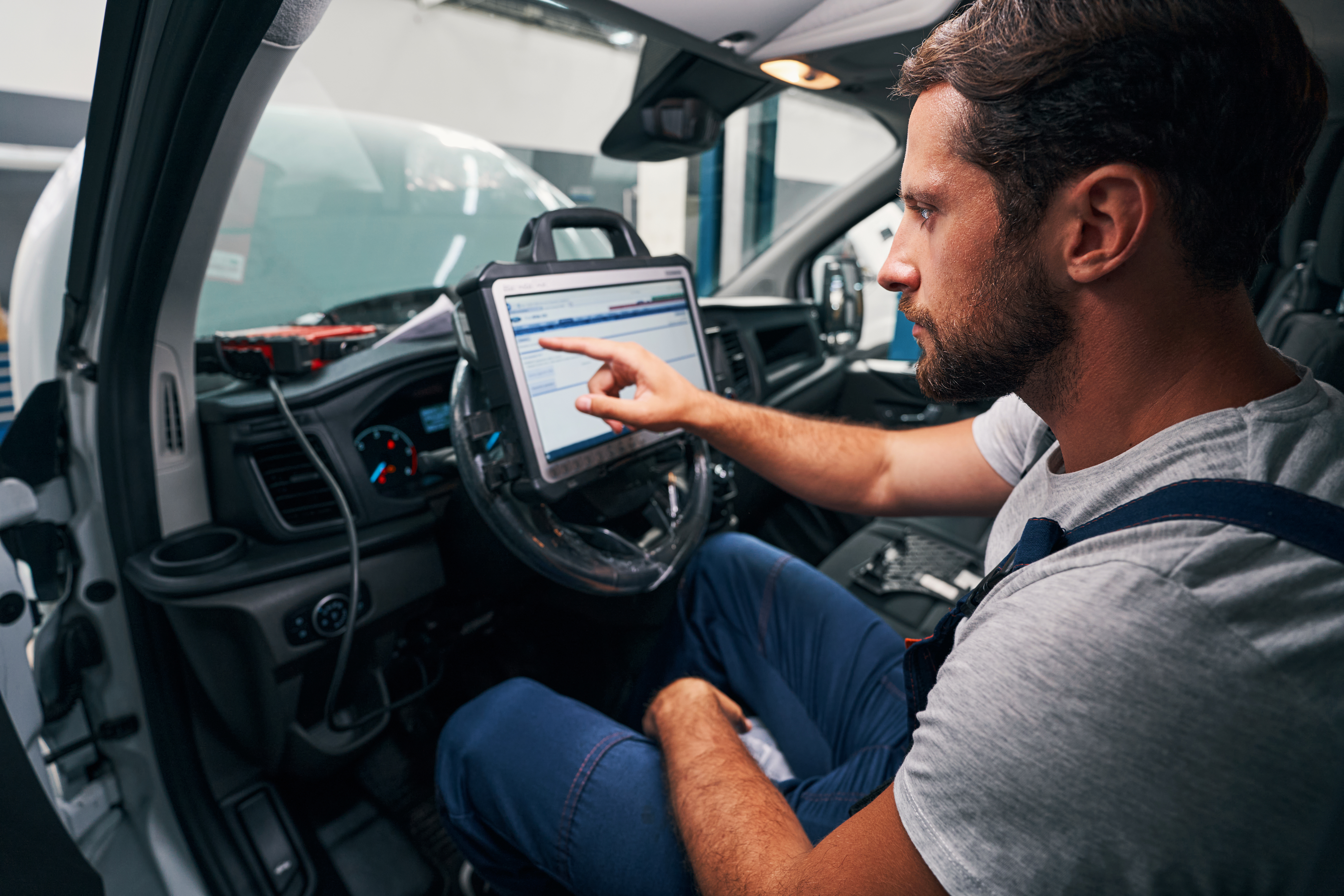 Auto technician using diagnostic tablet inside vehicle dashboard