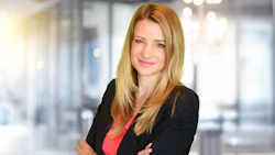 Professional woman in black blazer and coral top standing confidently in office