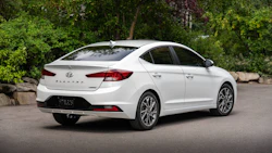 White Hyundai Elantra sedan parked on asphalt with green foliage background